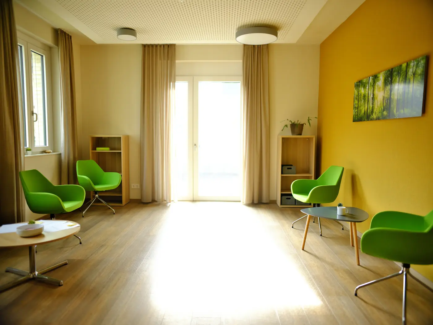 heller, freundlicher Raum. großes Fenster, grüne Sessel und gelbe Wände
