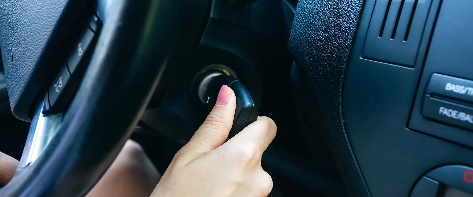 Nahaufnahme von einem Lenkrad und einer femininen Hand, die den Schlüssel umdreht, um das Auto zu starten