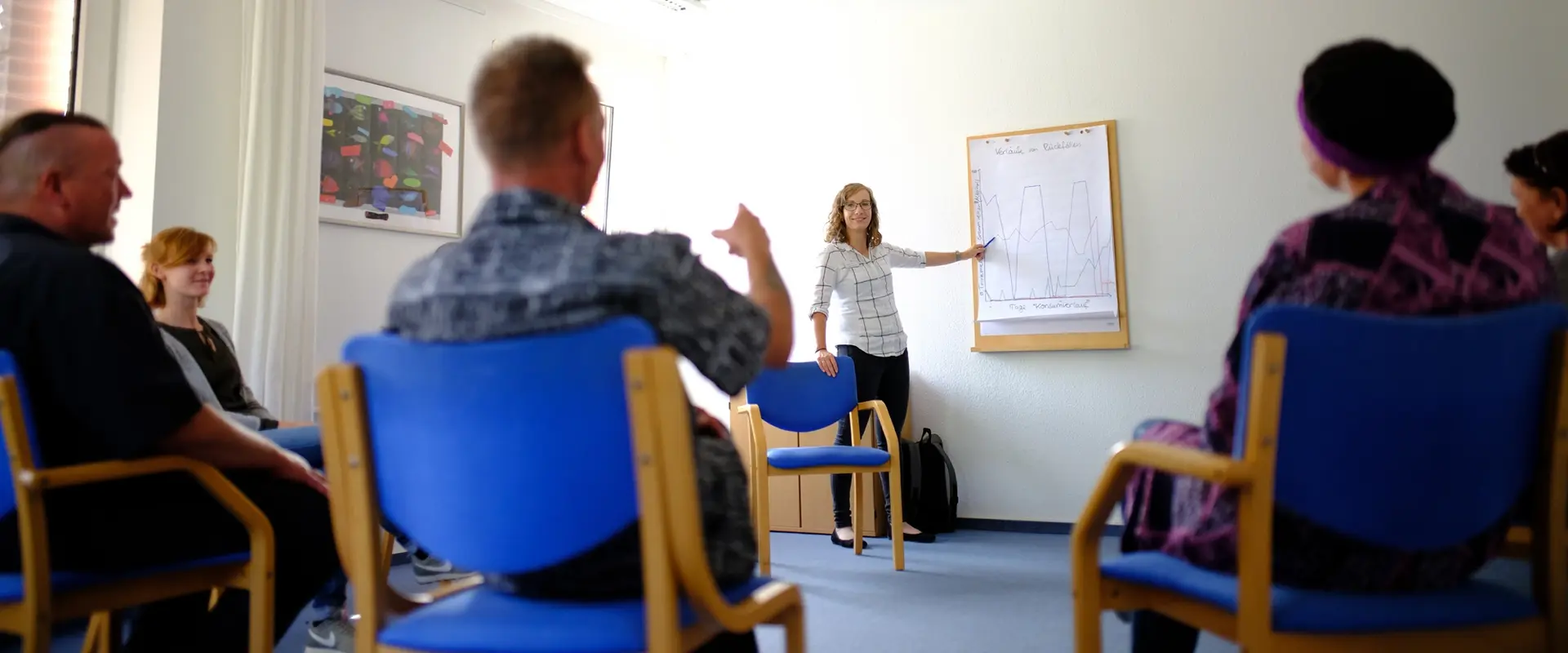 Gruppenstunde mehrere Menschen sitzen im Kreis, eine Mitarbeiterin erklärt etwas 