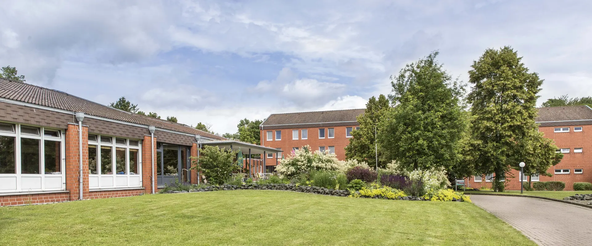 Panorama Bild der Fachklinik Erlengrund. Roter Klinkerbau und eine Parkanlage mit großen Bäumen 